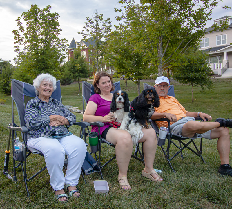 Three people sitting in lawn chairs with two dogs in a park in stephens valley