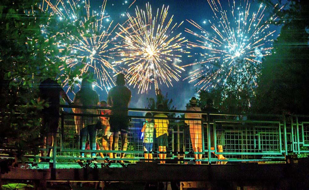 A group of people gathered on a bridge with fireworks going off in the distance